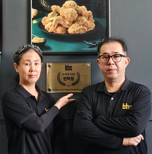 ▲bhc치킨 민락점 신영진 점주(오른쪽) 부부가 장기운영 현판 앞에서 포즈를 취하고 있다