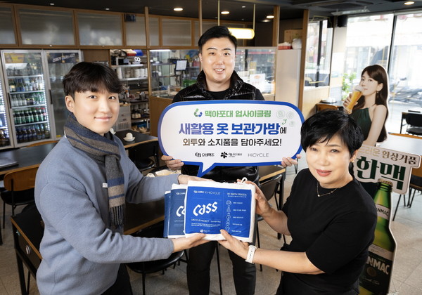 ▲오비맥주가 맥아포대로 제작한 ‘새활용 외투 보관가방’을 제작해 소상공인들에게 전달했다. 족발상회 방이점 점장(오른쪽)과 오비맥주 영업 담당자들이 기념 사진을 찍고 있다