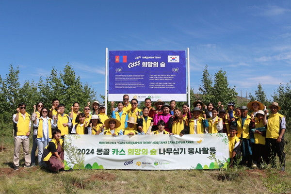 ▲ 지난 24일 오비맥주 임직원들이 푸른아시아 관계자, 몽골 환경난민 등으로 구성된 봉사단과 몽골 ‘카스 희망의 숲’ 기념 현판 앞에서 나무심기 봉사활동을 마치고 기념사진을 찍고 있다